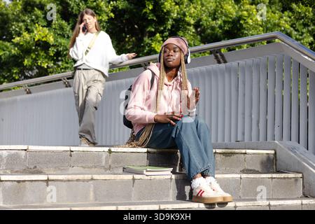 Diverse female students sitting and standing on concrete campus steps with backpack and smartphone Stock Photo