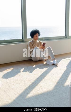 Man leaning against wall on rug overlooking ocean while using smartphone, copy space Stock Photo
