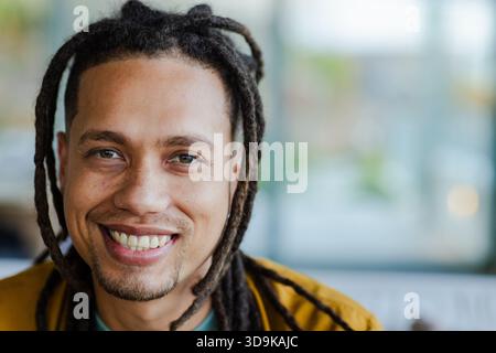 African American man smiling broadly at camera in lounge wearing mustard jacket over green shirt Stock Photo