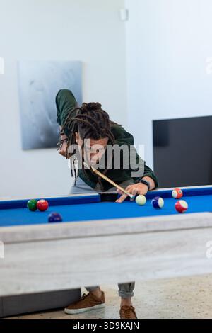 African American man aiming cue ball on blue-felt pool table using cue stick at home Stock Photo