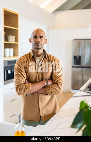 Asian man standing with arms folded in modern kitchen by marble countertop near coffee machine Stock Photo