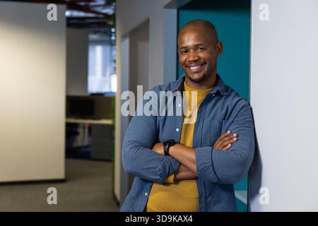 African American man leaning on wall in office corridor wearing smartwatch beside computer monitor Stock Photo