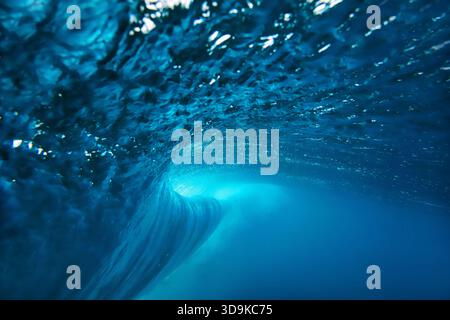 Underwater view breaking ocean wave tunnel deep blue barrel curling above, light filtering through translucent Stock Photo