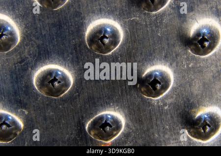 Macro close up texture view of a stainless steel metal kitchen grater surface with sharp perforated holes. Stock Photo