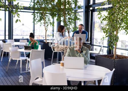 African American man working on laptop with coffee cup at shared workspace overlooking waterfront Stock Photo