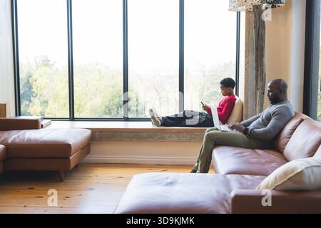 African American father and son working on laptop and using smartphone in living room, copy space Stock Photo