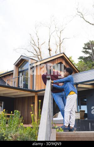 African American father and son talking while leaning on wooden railing at wood-clad house entrance Stock Photo