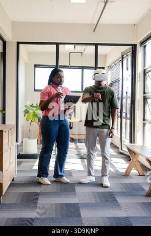 African American colleagues using tablet while man wearing white VR headset in glass meeting room Stock Photo