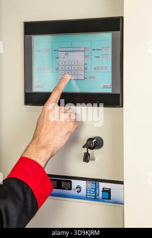 A  hand, wearing a dark garment with a red cuff, presses a numeric key on a touchscreen control panel of a machine or laboratory apparatus Stock Photo
