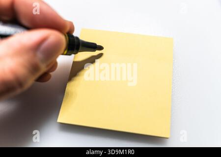 Marker in hand over empty yellow sticky note on white background Stock Photo