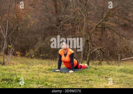 Woman performing yoga stretching on a mat in a park setting Stock Photo