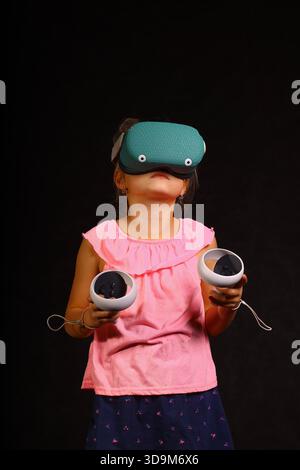 Child using virtual reality headset with motion controllers during immersive VR gaming experience on dark studio background Stock Photo