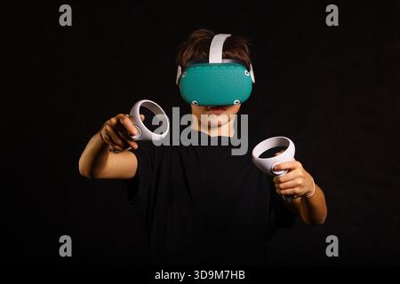 Boy engaged in virtual reality game, holding both controllers forward while concentrating on gameplay. Stock Photo