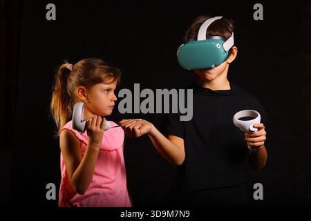 Siblings Interacting with Virtual Reality Headset and Controllers Indoors Stock Photo