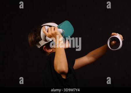 Boy lifting VR headset while holding controller, exploring virtual world and interactive gaming technology. Stock Photo