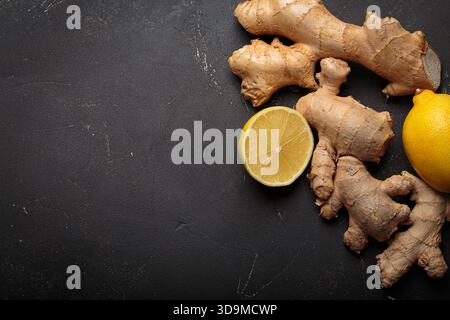 Ginger roots and whole and cut lemons creating a natural remedy concept. Healthy raw ingredients on dark textured surface space for text Stock Photo