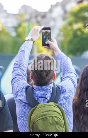 A man holds his smartphone high above a crowd, recording a live event and symbolizing the modern fusion of technology, social media sharing and the co Stock Photo