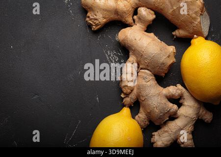Ginger roots and whole and cut lemons creating a natural remedy concept. Healthy raw ingredients on dark textured surface space for text Stock Photo
