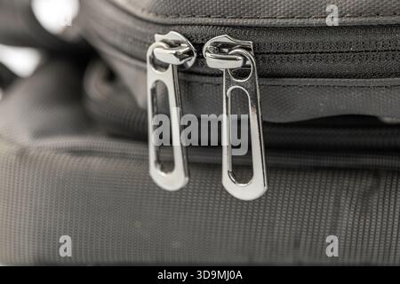 A close-up view of two shiny metal zipper pulls on a black fabric bag. The zippers are positioned side by side, showcasing their sleek design against Stock Photo