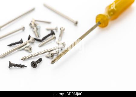 A close-up view of a yellow-handled screwdriver lying next to a diverse assortment of screws on a clean white background. Stock Photo