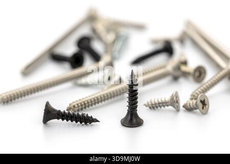 A collection of different screws scattered across a white surface, showcasing various types including metal, black, and silver screws. Stock Photo
