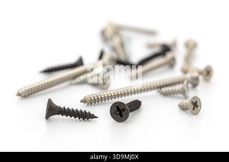A collection of various screws lies scattered on a clean white surface, showcasing different sizes and finishes. Some screws display a shiny metallic Stock Photo