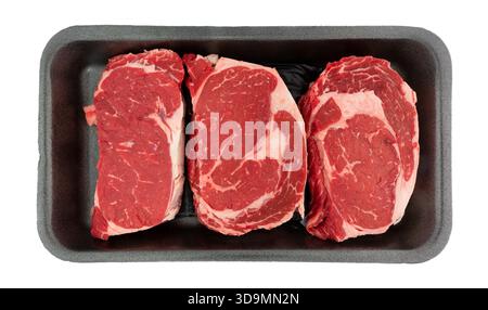 Overhead view of three ribeye steaks in a black foam retail meat tray on a white background. Stock Photo