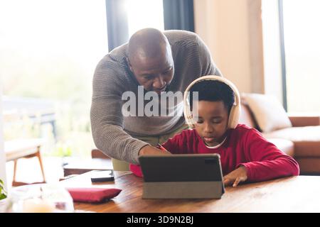African American father and son working using tablet and stylus with headphones in home living room Stock Photo