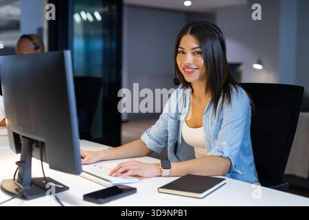 Indian woman wearing headset sitting at desk in office typing on computer copy space Stock Photo