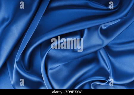 Crumpled, wrinkled blue colored glossy silk satin with wave drapery.. Shiny smooth fabric with soft folds, cloth texture . Elegant rich background, wa Stock Photo