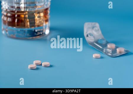 A blurred glass of alcohol in the background and a pack of pills. Three pink tablets are sitting on the table ready to use. Focus on foreground Stock Photo