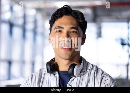 Asian man standing in bright office wearing striped shirt and navy tee sporting wireless headphones Stock Photo