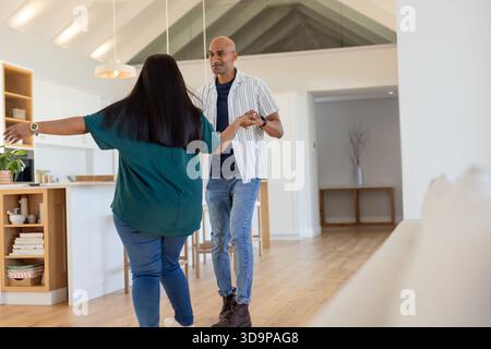 Diverse couple dancing together in open-plan home area near kitchen island and pendant lights Stock Photo