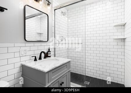 A bathroom with a grey cabinet with a white subway tile backsplash and tiled shower with a glass sliding door. Stock Photo