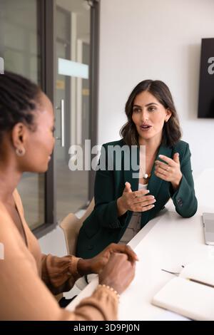 Positive young Latin businesswoman talking to partner at workplace Stock Photo