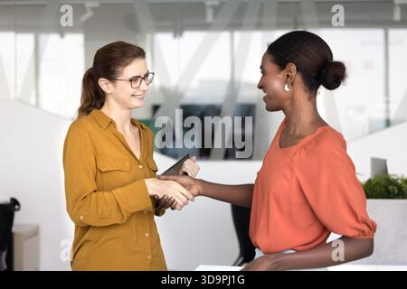 Positive multiethnic female startup colleagues shaking hands Stock Photo