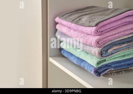 Neatly stacked multicolored towels on shelf for bathroom organization and decoration. Stock Photo