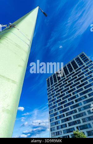 Low-angle view of a streetlight and a modern high-rise building against a deep blue sky with light clouds. Stock Photo