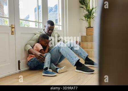 Mid-adult African American father holding child, comforting on hardwood floor by front glass door Stock Photo