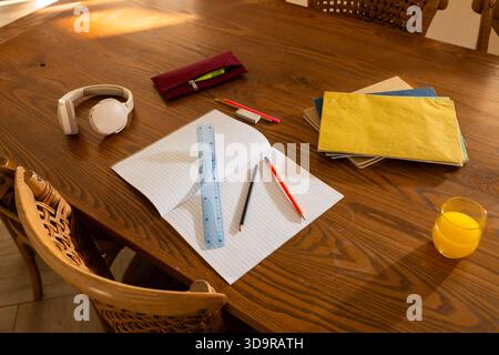 Open lined notebook sitting centered on wooden dining table with blue ruler and pencils Stock Photo