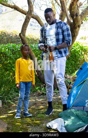 African American father wearing blue plaid and child wearing yellow shirt packing cookware by tent Stock Photo