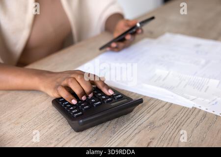 Black woman using calculator and smartphone for personal financial audit Stock Photo