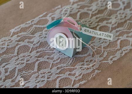 Lovingly wrapped small gift package for confirmation with ribbon and a lettering GRATULATION means congratulation on a white decorated wooden table an Stock Photo