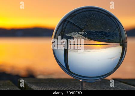 A round glass ball reflects the sunset in early summer on the beach bridge, the beach pier in Solitüde near Flensburg on the Baltic Sea in the Flensbu Stock Photo