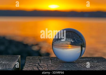 A round glass ball reflects the sunset in early summer on the beach bridge, the beach pier in Solitüde near Flensburg on the Baltic Sea in the Flensbu Stock Photo