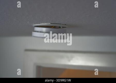 A view of a smoke detector mounted on a ceiling, showcasing its circular design and white color against a light background. Stock Photo