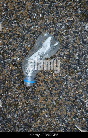 A discarded plastic bottle lies on a textured asphalt surface, highlighting environmental pollution. Stock Photo