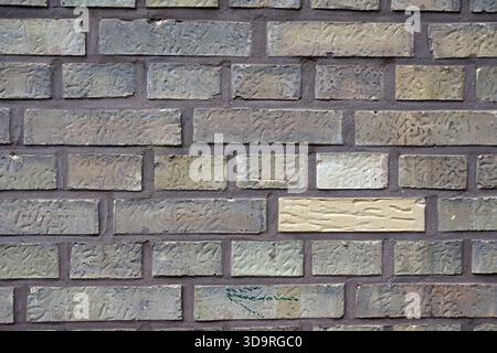 A structured wall built from alternating rows of long and small bricks in muted greyish tones with one vivid yellow and one white brick standing out. Stock Photo