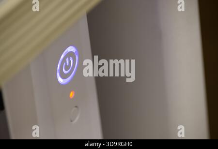 A glowing power button on an electronic device, with a blue LED light indicating it's on, and a small red light below it. Stock Photo