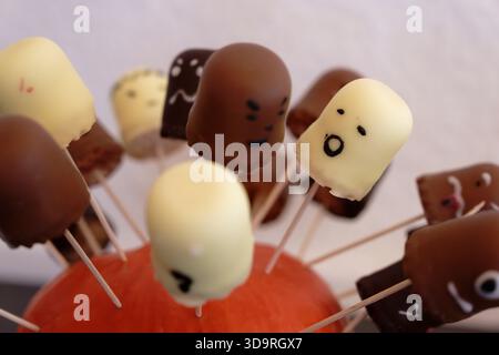 White and cream colored candies on wooden sticks, each with drawn faces smiling, surprised, happy. A cute and playful Halloween themed treat. Stock Photo